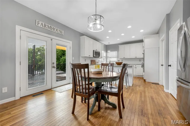 Open-concept kitchen and dining area featuring wood-finish flooring, white cabinetry, stainless steel appliances, and a tiled backsplash — 501 Oxborough Court, Cottleville, MO 63376