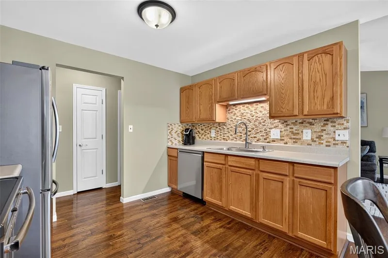 Kitchen featuring wood-finish flooring, a tiled backsplash, wood cabinetry, stainless steel appliances, and a recessed sink with a gooseneck faucet — 30 Hunting Manor Drive, St Charles, MO 63303