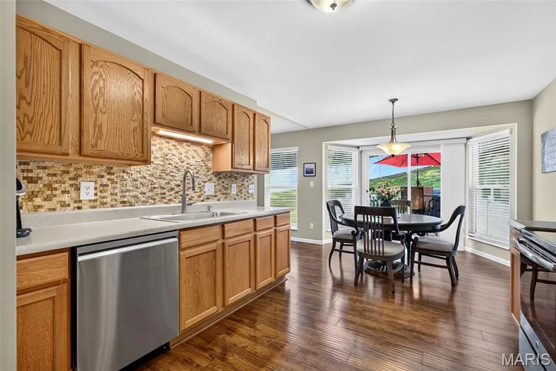 Kitchen featuring wood cabinetry, stainless steel dishwasher, mosaic tile backsplash, and light-toned countertops — 30 Hunting Manor Drive, St Charles, MO 63303