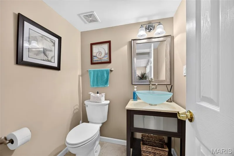 Compact bathroom featuring a white toilet, a dark wood-finish vanity with a light-colored countertop, and a vessel sink — 30 Hunting Manor Drive, St Charles, MO 63303