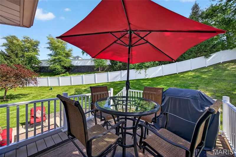 Exterior deck featuring wood-finish flooring, white railing, and a sloped grassy yard with mature trees — 30 Hunting Manor Drive, St Charles, MO 63303