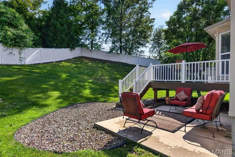 Expansive outdoor living area featuring a ground-level patio, a raised deck with white railings, a gravel landscaping bed, and a sloped lawn area — 30 Hunting Manor Drive, St Charles, MO 63303