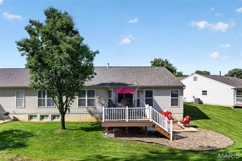 Rear exterior featuring a spacious wooden deck with white railings and stairs, a lower-level gravel patio, and an expansive sloped lawn — 30 Hunting Manor Drive, St Charles, MO 63303