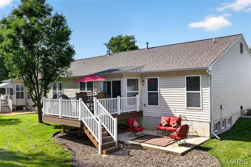 Two-tier outdoor living space featuring a raised deck with white railings and stairs, a ground-level concrete patio, and a manicured lawn — 30 Hunting Manor Drive, St Charles, MO 63303