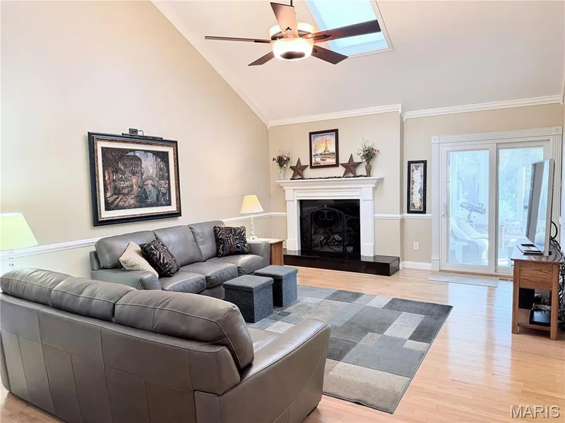 Vaulted ceiling with skylight, wood-finish flooring, fireplace with white mantel, two-tone wall treatment, and sliding glass doors — 14238 Kinderhook Drive, Chesterfield, MO 63017