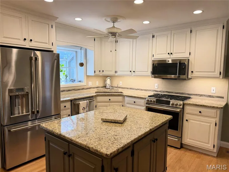Kitchen featuring stainless steel appliances, a central island with a granite-style countertop, white cabinetry with black hardware, and wood-finish flooring — 14238 Kinderhook Drive, Chesterfield, MO 63017