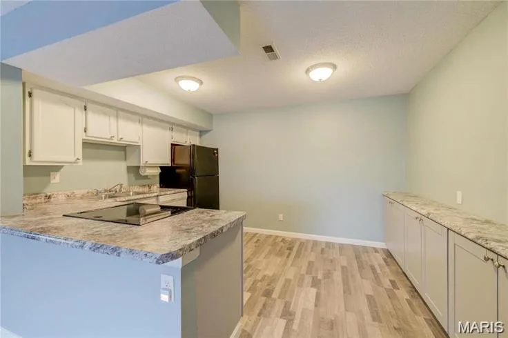 Compact kitchen area featuring a built-in cooktop, undermount sink, white cabinetry, and a refrigerator — 1430 Summergate Parkway #J, St Charles, MO 63303