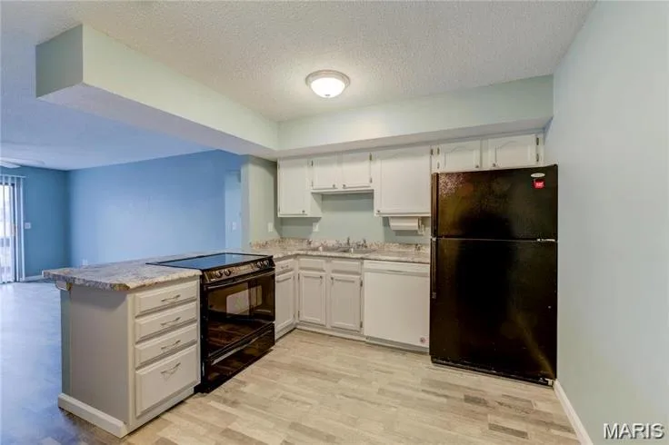 Kitchen featuring wood-finish flooring, an island with integrated cooktop, light-toned cabinetry, and light-colored countertops — 1430 Summergate Parkway #J, St Charles, MO 63303