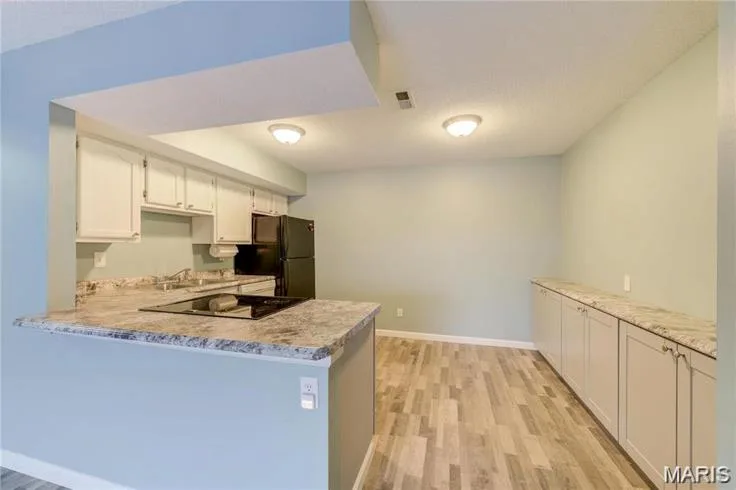 Kitchen and dining area featuring white cabinetry, wood-finish flooring, and speckled countertops — 1430 Summergate Parkway #J, St Charles, MO 63303