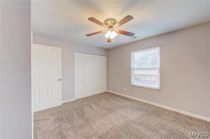 Carpeted room featuring a ceiling fan with light fixture, a window with blinds, and white bi-fold closet doors — 1430 Summergate Parkway #J, St Charles, MO 63303