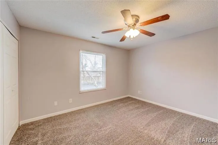 Neutral-toned room featuring a window with blinds, a ceiling fan with light fixture, textured carpeting, and a bi-fold closet door — 1430 Summergate Parkway #J, St Charles, MO 63303