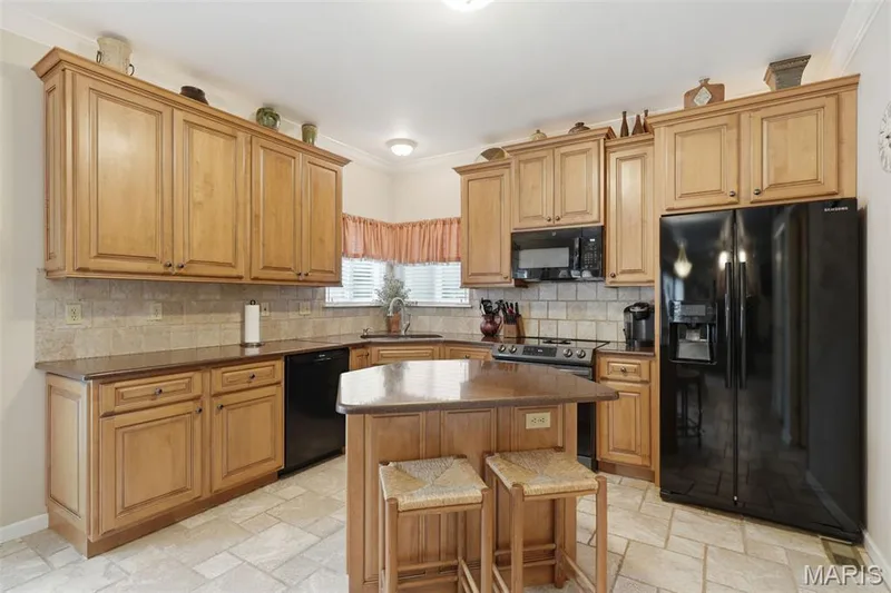 Kitchen featuring maple wood cabinetry, a central island with seating, Silestone countertops, tile backsplash, and porcelain floor tile — 28 Seabiscuit Drive, St Charles, MO 63301