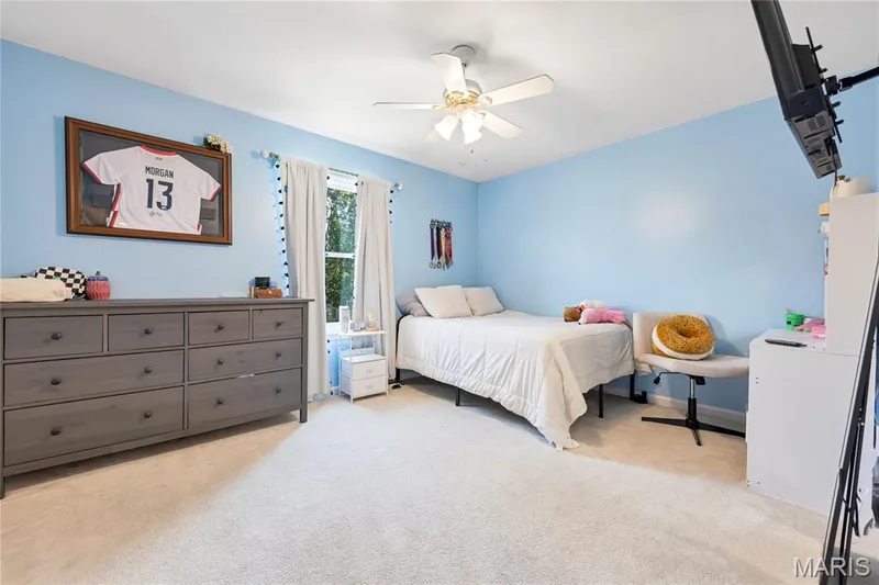 Carpeted room featuring a ceiling fan, a window with curtains, and views of the back yard. — 2304 Bear Fountain Run, Wentzville, MO 63385