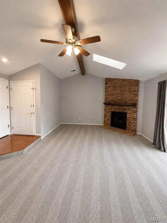 Vaulted ceiling with exposed wood beam, ceiling fan with light, skylight, brick-surround fireplace with wood mantel, and light-tone carpet flooring — 974 Windstream Drive #38, St Peters, MO 63376
