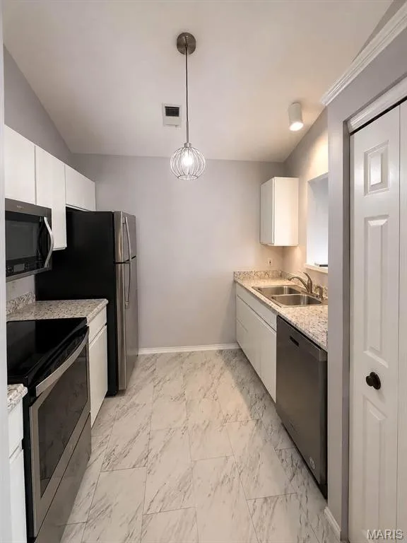 Stainless steel appliances, light-toned countertops, white cabinetry, tile flooring, and a decorative pendant light — 974 Windstream Drive #38, St Peters, MO 63376