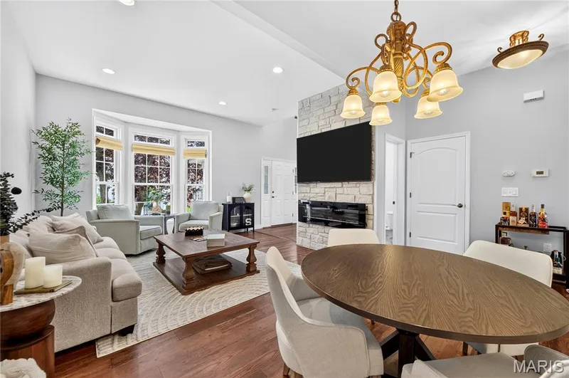 Open-concept living space featuring wood-finish flooring, a stone-clad fireplace with built-in electric fireplace, and a multi-light chandelier — 2514 S Larksong Drive, Grover, MO 63040