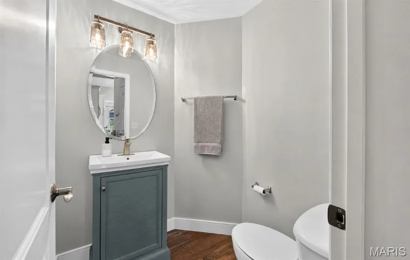 Powder room featuring a vanity with an integrated sink, an oval mirror, and a three-light vanity fixture with clear glass shades — 2514 S Larksong Drive, Grover, MO 63040