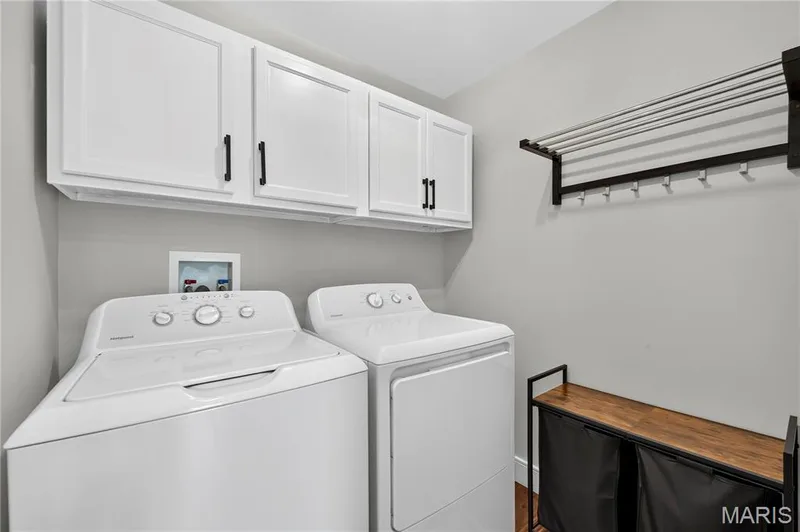 Main Floor off of Half bath Laundry area featuring white cabinetry with dark hardware, a wall-mounted drying rack, and wood-finish flooring — 2514 S Larksong Drive, Grover, MO 63040