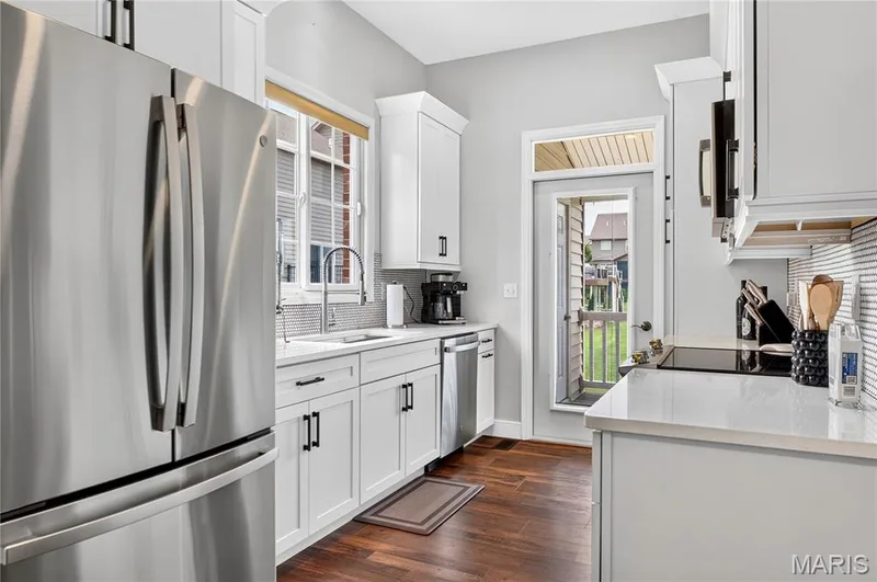Modern kitchen featuring stainless steel appliances, white cabinetry with matte black hardware, stone countertops, and wood-finish flooring — 2514 S Larksong Drive, Grover, MO 63040