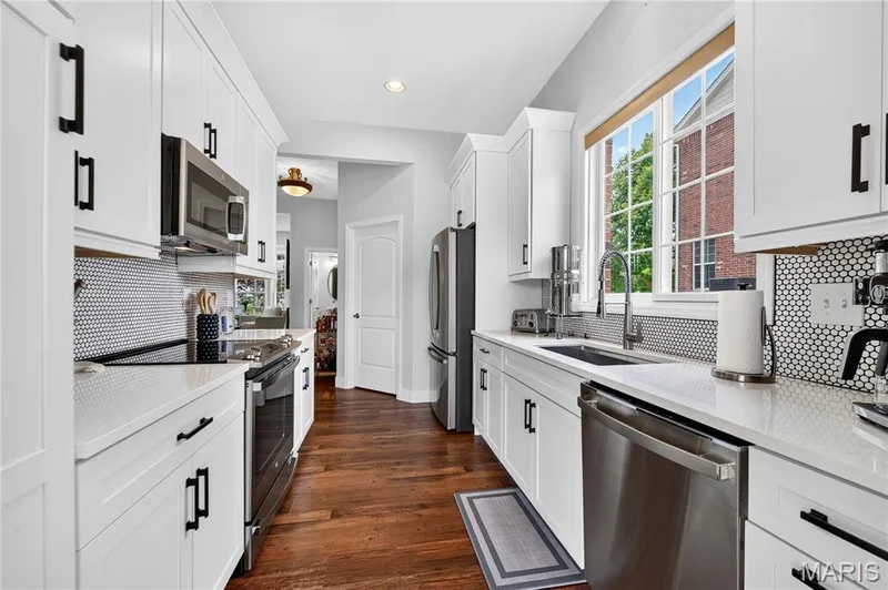 Galley kitchen featuring white cabinetry, stainless steel appliances, a black penny tile backsplash, white countertops, and wood-finish flooring — 2514 S Larksong Drive, Grover, MO 63040