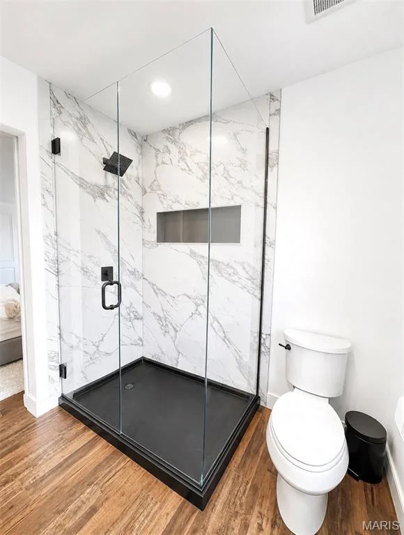 Frameless glass shower enclosure featuring white marble-look walls, a built-in shower niche, and a matte black shower head and door hardware — 2514 S Larksong Drive, Grover, MO 63040