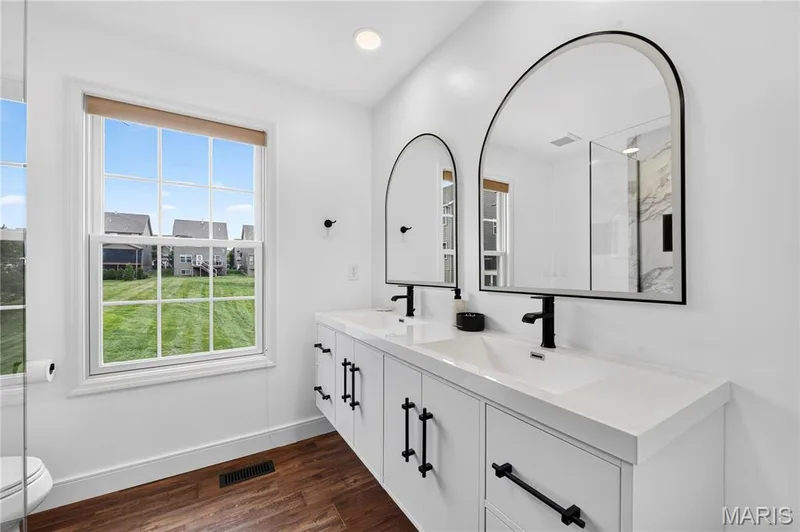 Dual vanity featuring white cabinetry, lighted mirrors, cabinet underlighting, integrated sinks, and matte black hardware — 2514 S Larksong Drive, Grover, MO 63040