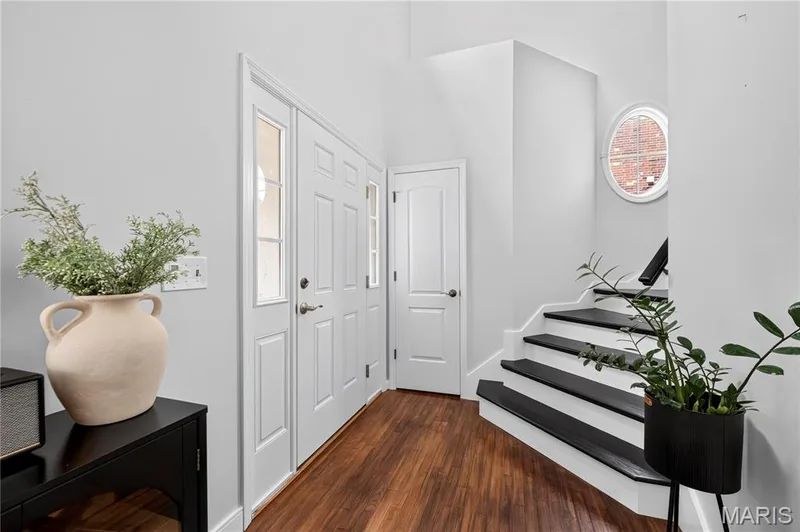 Entryway featuring wood-finish flooring, white paneled doors, and a staircase with dark treads and white risers — 2514 S Larksong Drive, Grover, MO 63040