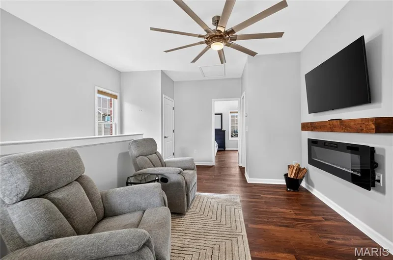 Loft space featuring wood-finish flooring, a contemporary ceiling fan, and an electric fireplace with a rustic wood mantel — 2514 S Larksong Drive, Grover, MO 63040