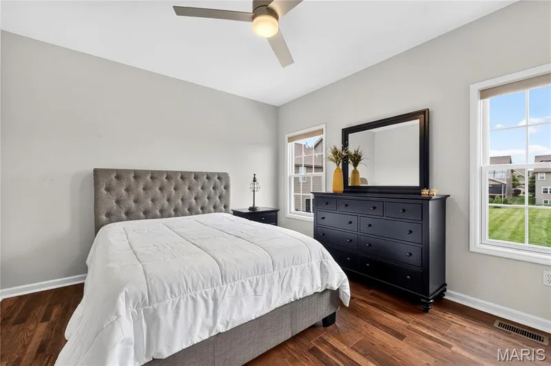 Bedroom featuring wood-finish flooring, two large windows with mullions, a ceiling fan with integrated lighting, and light-toned wall paint — 2514 S Larksong Drive, Grover, MO 63040