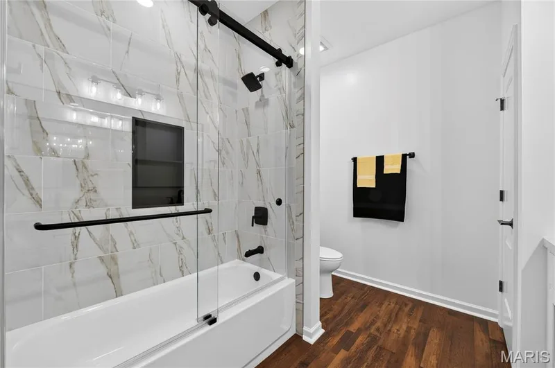 Full bathtub with a glass shower enclosure and matte black hardware, featuring a tiled surround with a built-in shower niche — 2514 S Larksong Drive, Grover, MO 63040