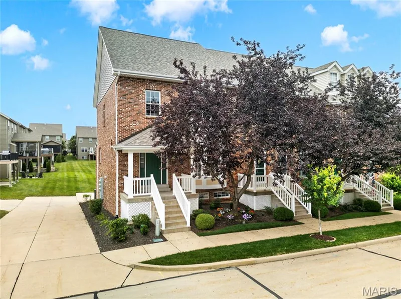 Brick facade townhome with covered entry porch, white railings, and mature front landscaping — 2514 S Larksong Drive, Grover, MO 63040