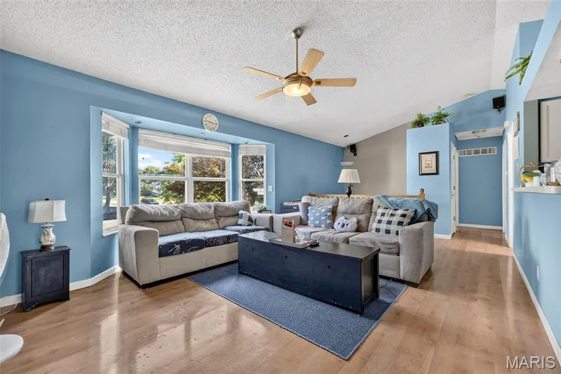 Spacious living area featuring a large bay window, vaulted ceiling, and wood-finish flooring — 17 Kingspointe Court, St Peters, MO 63376