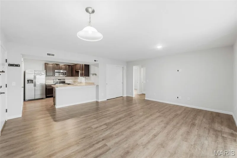 Spacious open-concept living area featuring LVP flooring, and a kitchen with dark cabinetry, stainless steel appliances, and a breakfast bar — 321 Bordeaux Way, St Peters, MO 63376