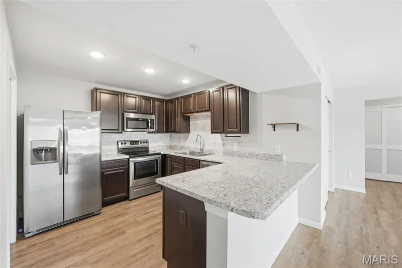 Kitchen featuring an extended island with a light-colored countertop, dark wood-finish cabinetry, stainless steel appliances, and wood-finish flooring — 321 Bordeaux Way, St Peters, MO 63376