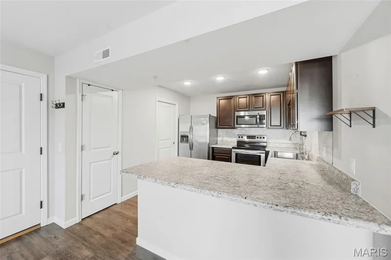 Kitchen featuring a breakfast bar with stContemporary kitchen featuring LVP flooring, dark wood cabinetry, backsplash, and stainless steel appliances-- refrigerator INCLUDED! — 321 Bordeaux Way, St Peters, MO 63376