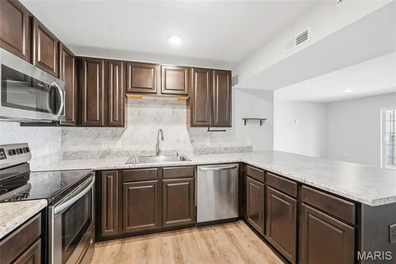 Contemporary kitchen featuring LVP flooring, dark wood cabinetry, backsplash, and stainless steel appliances-- refrigerator INCLUDED! — 321 Bordeaux Way, St Peters, MO 63376