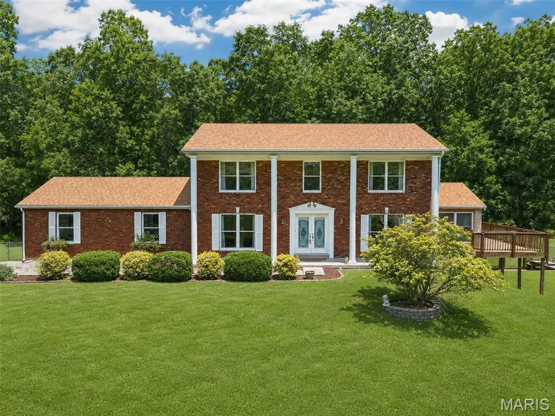 Traditional brick-front residence featuring a spacious front lawn, white columned portico, and a prominent deck extension — 3672 Hawks Rest Road, Wildwood, MO 63069