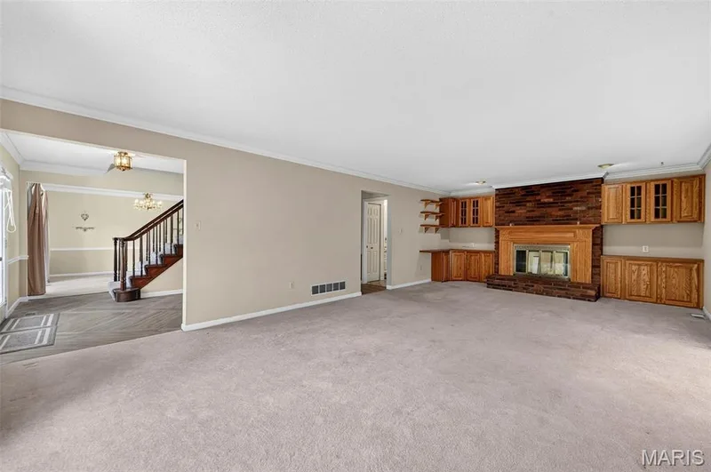 Spacious living area featuring a brick-surround fireplace with a wood mantel, built-in cabinetry, and neutral carpeting — 3672 Hawks Rest Road, Wildwood, MO 63069