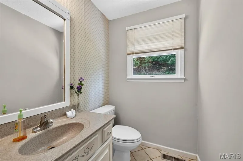 Bathroom vanity featuring an integrated sink, framed mirror, and patterned wallpaper — 3672 Hawks Rest Road, Wildwood, MO 63069