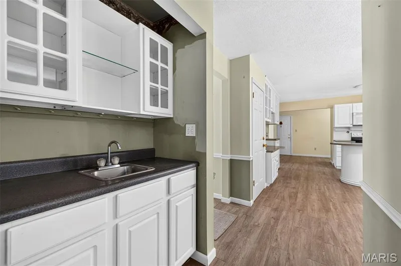Wet bar featuring white cabinetry, glass-front upper cabinets, a stainless steel sink, and dark countertops — 3672 Hawks Rest Road, Wildwood, MO 63069