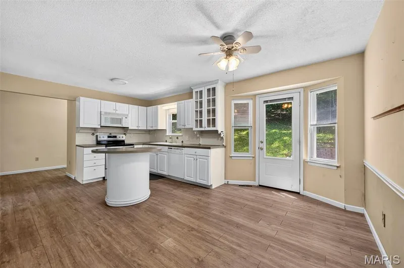 Kitchen featuring white cabinetry, a built-in microwave, a black electric range, a curved island with a dark countertop, and wood-finish flooring — 3672 Hawks Rest Road, Wildwood, MO 63069