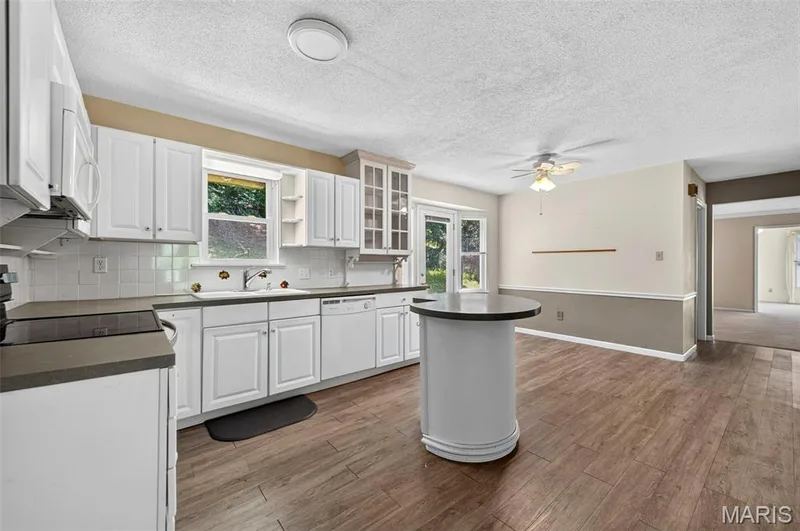 Kitchen featuring wood-finish flooring, white cabinetry, dark countertops, a circular island, and a tile backsplash — 3672 Hawks Rest Road, Wildwood, MO 63069