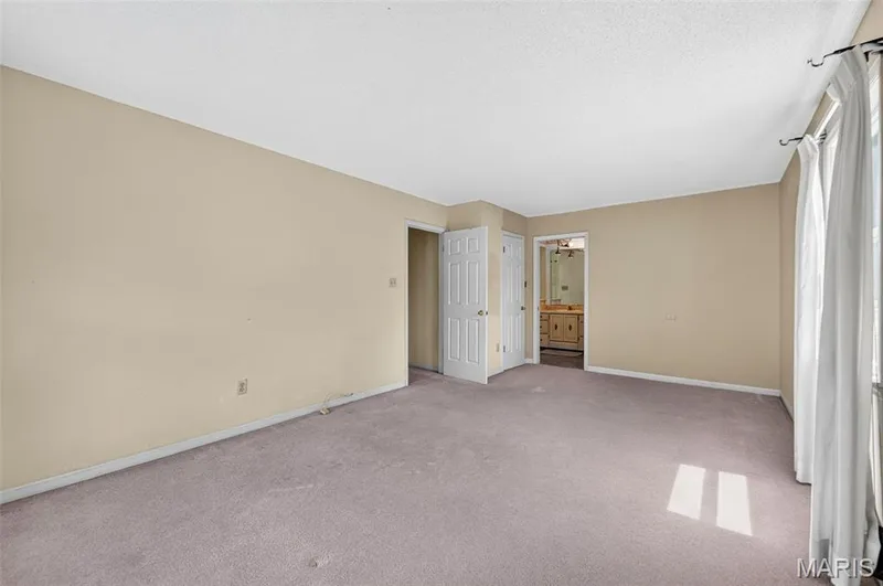 Spacious carpeted room featuring a white ceiling, light beige walls, a window with curtains, and two interior doors — 3672 Hawks Rest Road, Wildwood, MO 63069
