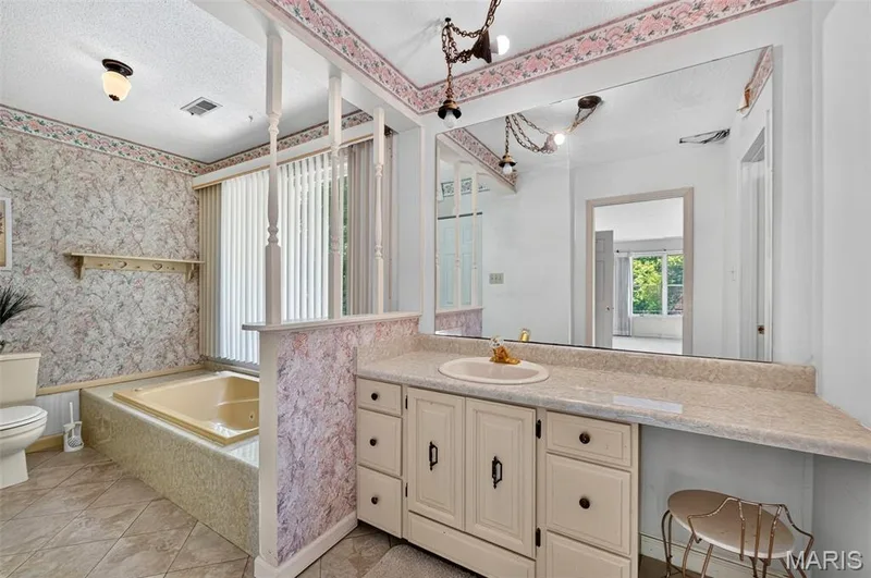 Bathroom featuring a built-in jetted tub, single vanity with integrated sink, expansive wall mirror, and tile flooring — 3672 Hawks Rest Road, Wildwood, MO 63069