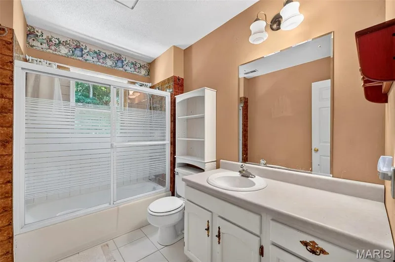 Bathroom featuring a built-in tub with a sliding glass shower door, a single vanity with an integrated sink, white base cabinetry, and a wall-mounted mirror — 3672 Hawks Rest Road, Wildwood, MO 63069