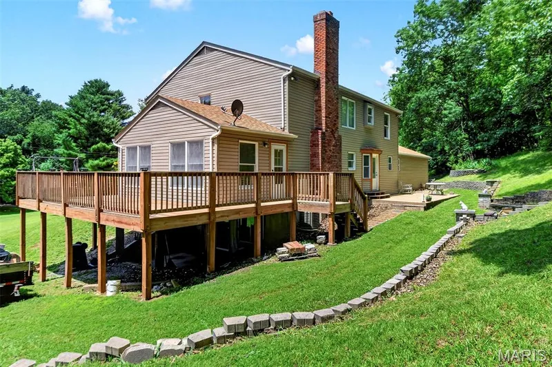 Rear exterior featuring a spacious wood deck, brick chimney, and a multi-level terraced yard — 3672 Hawks Rest Road, Wildwood, MO 63069
