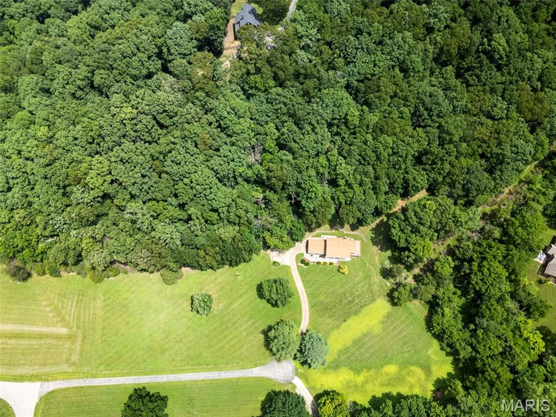 Aerial perspective showcasing a single-story dwelling with a light-colored roof, surrounded by extensive mature trees — 3672 Hawks Rest Road, Wildwood, MO 63069