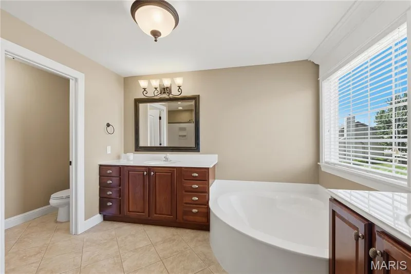 Spacious Primary Bathroom featuring a large soaking tub, tile flooring, and wood vanities — 5500 Wooded Creek Drive, O'Fallon, MO 63304
