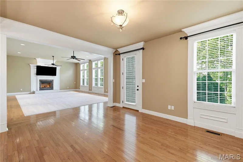 Large breakfast area looking towards the Great Room featuring wood flooring, large window surrounded by wood trim, and door which walks out to the patio area — 5500 Wooded Creek Drive, O'Fallon, MO 63304