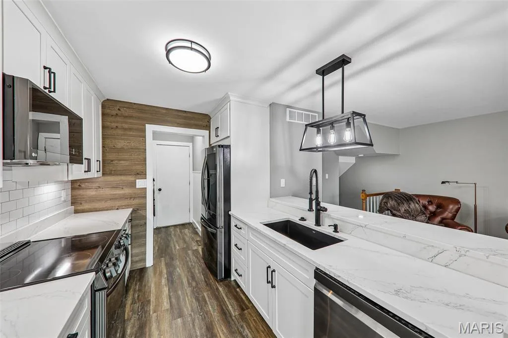 Contemporary kitchen featuring white cabinetry, quartz countertops, a shiplap accent wall, stainless steel appliances, and wood-finish flooring — 16180 Lea Oak Court, Chesterfield, MO 63017